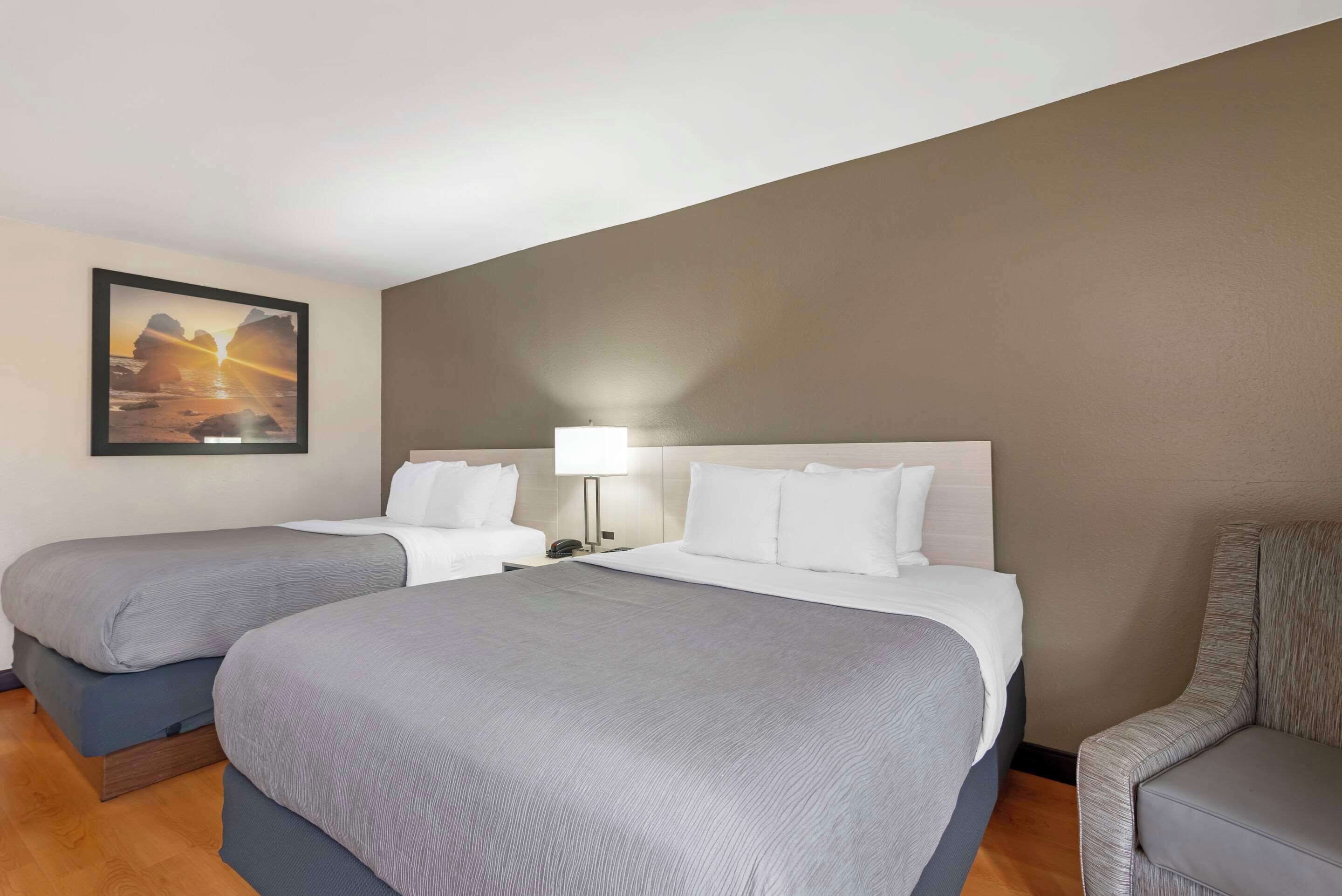 A hotel room with two beds, a nightstand, a lamp, and a framed picture on the wall.