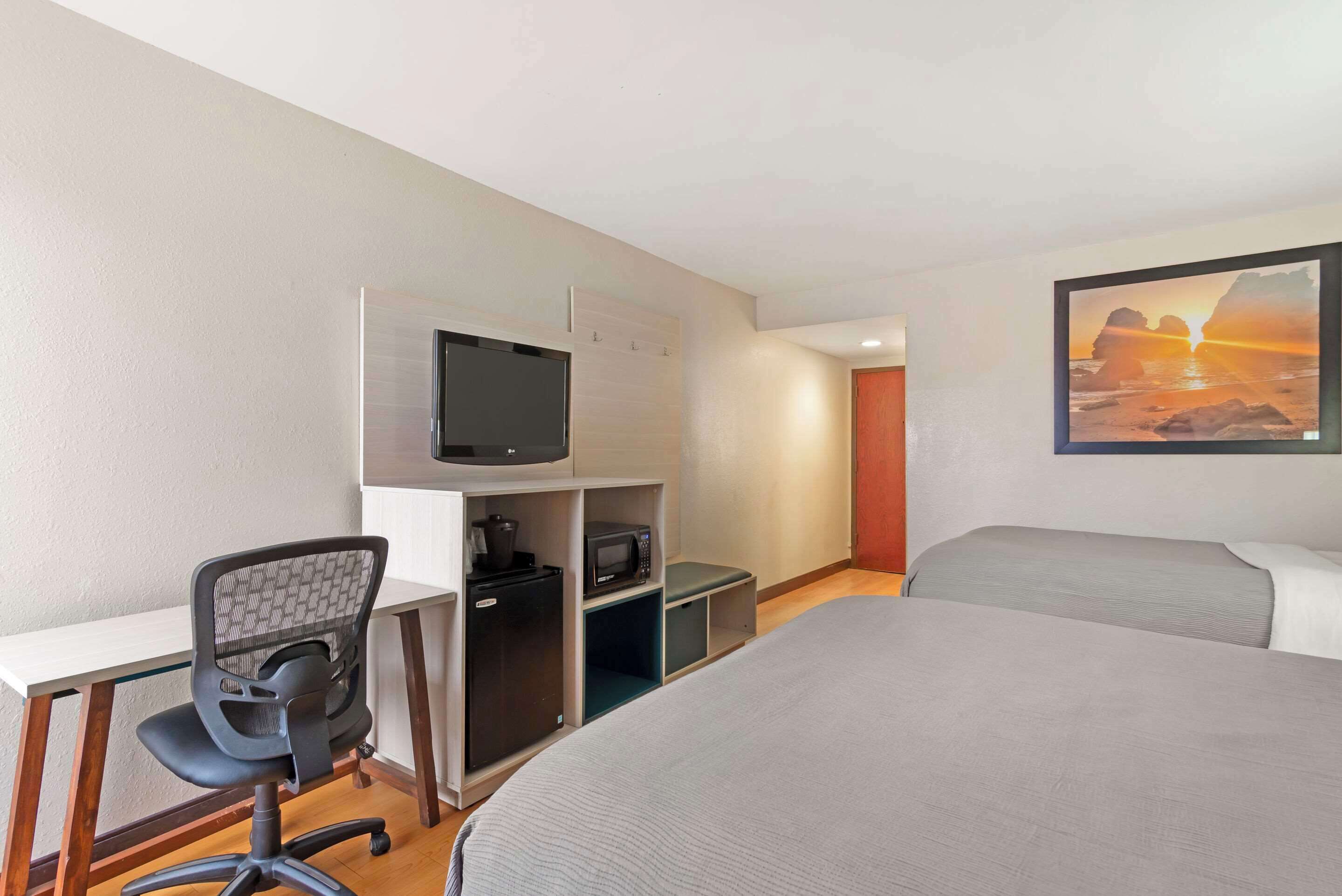 A hotel room with a bed, a desk with a chair, a television, a microwave, and a small refrigerator.