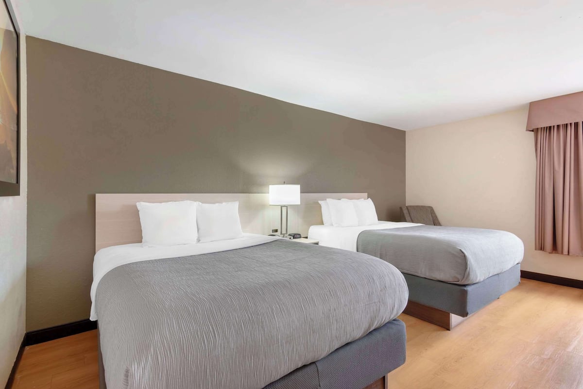Una habitación de hotel con dos camas, una mesita de noche con lámpara y un ventanal con cortinas.