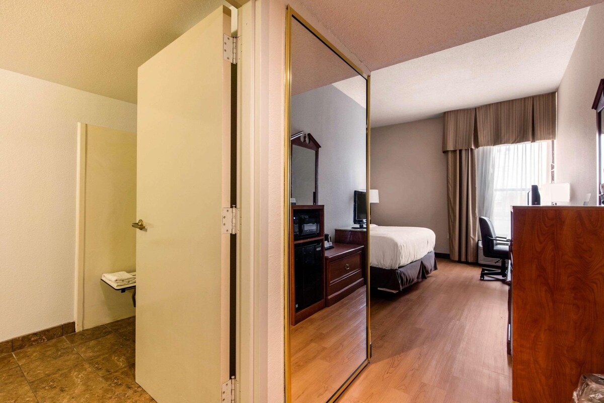 A hotel room with a wooden floor, a bed, a desk, a chair, a television, and a wardrobe.