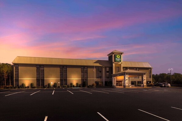 A large, modern hotel with a prominent 'Quality' sign, a spacious parking lot, and a well-lit entrance.