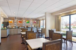 A modern restaurant with a kitchen area, dining tables, and chairs.
