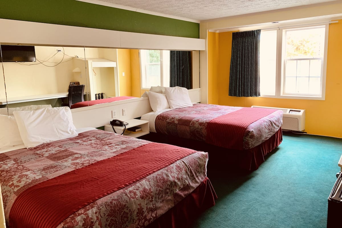 Habitación de hotel con dos camas, un escritorio, un espejo y una ventana con cortinas.
