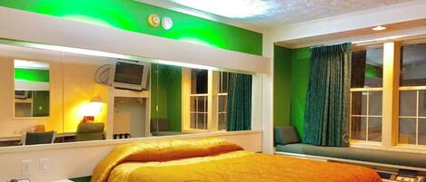 Quarto de hotel com cama, escrivaninha com telefone, televisão e janela com cortinas.