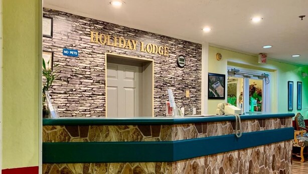 A reception desk at Holiday Lodge with a stone facade, a 'No Pets' sign, and a 'Check In' sign above the door. - Holiday Lodge (Greensboro)