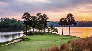 A golf course with a water body, trees, and a sunset. - Holiday Lodge (Greensboro)