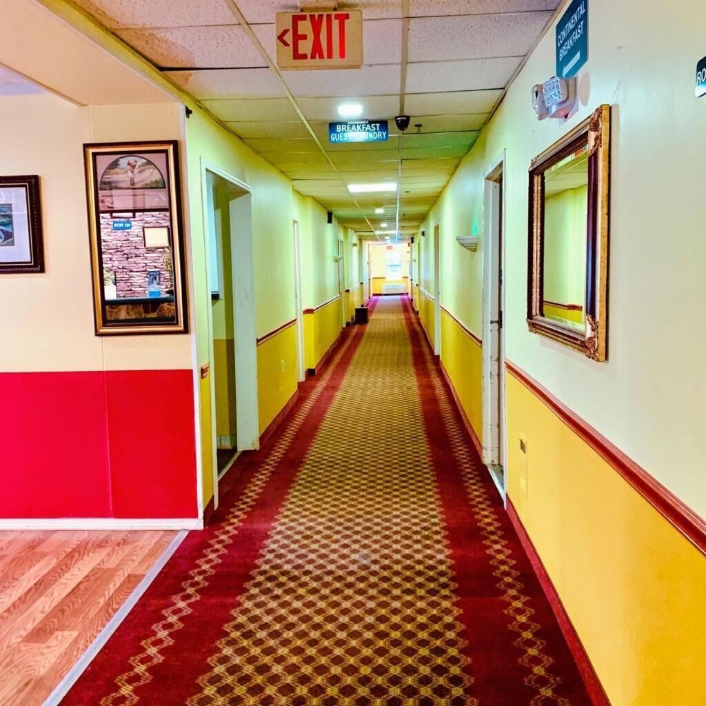 A hotel hallway with a red carpet, yellow walls, and an exit sign.