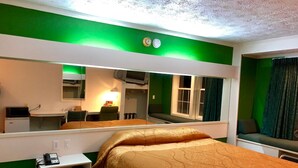 A hotel room with a large bed, a desk with a telephone, a mirror, and a window with curtains. - Holiday Lodge (Greensboro)