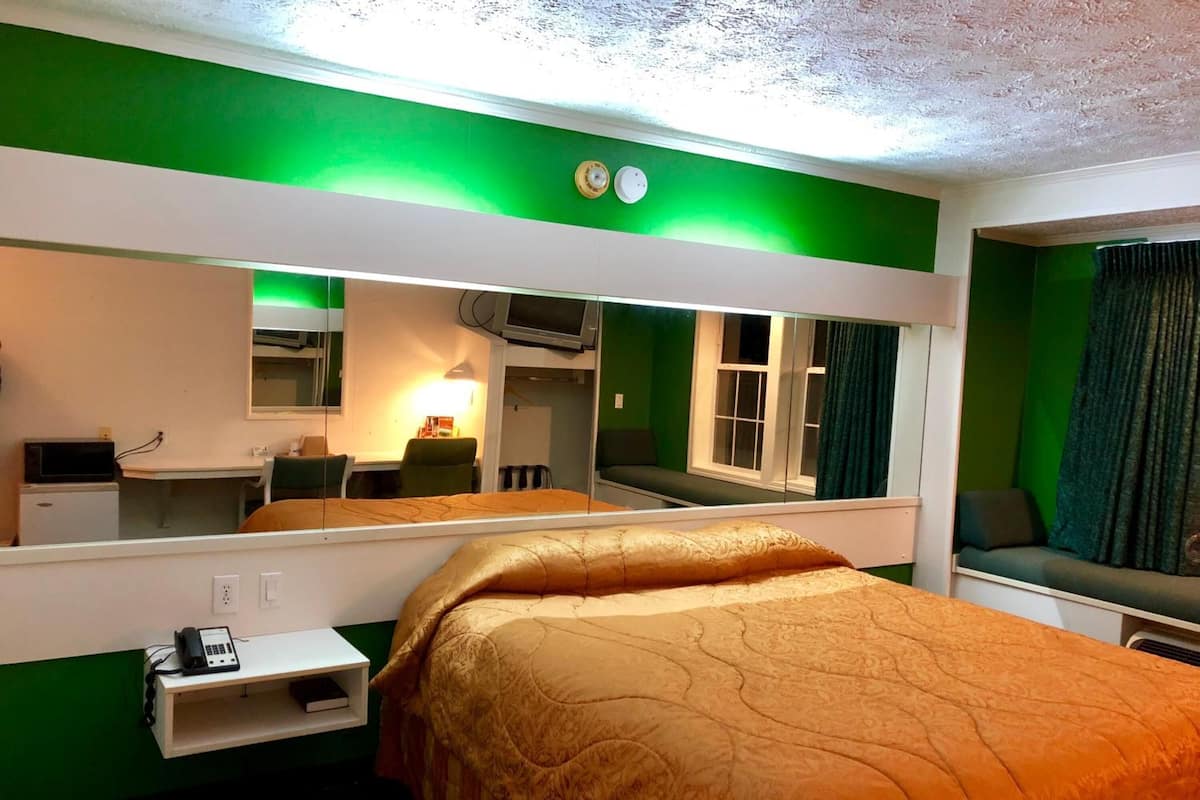 Habitación de hotel con una cama grande, un escritorio con teléfono, un espejo y una ventana con cortinas.
