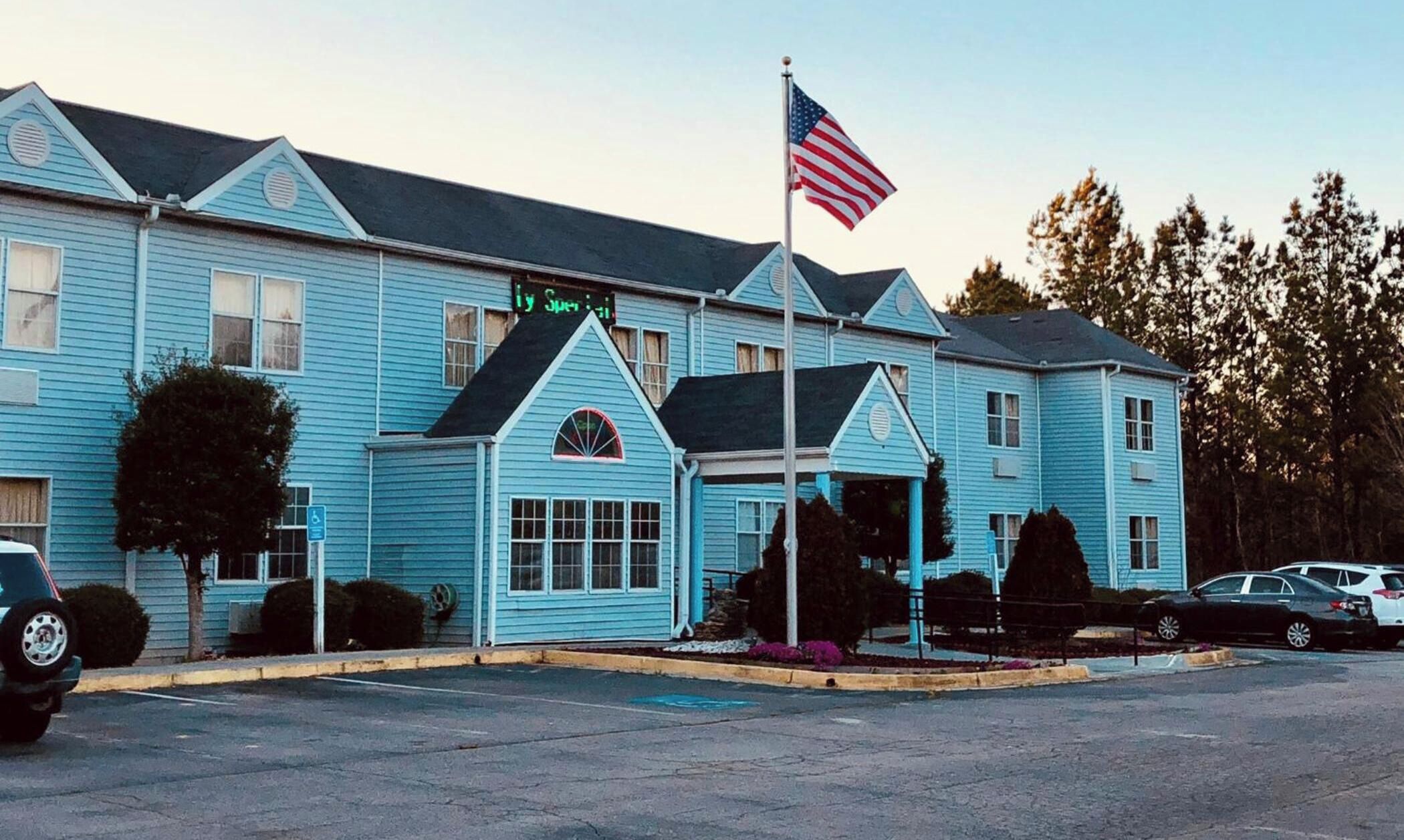 Un hotel de dos pisos con fachada azul, una bandera estadounidense y un letrero que indica un spa.