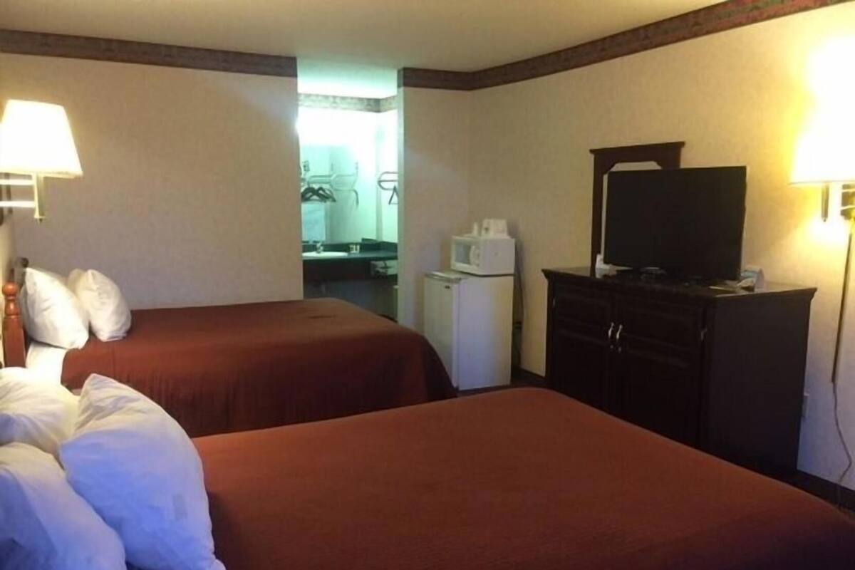 A hotel room with two beds, a television, a small refrigerator, and a mirror.