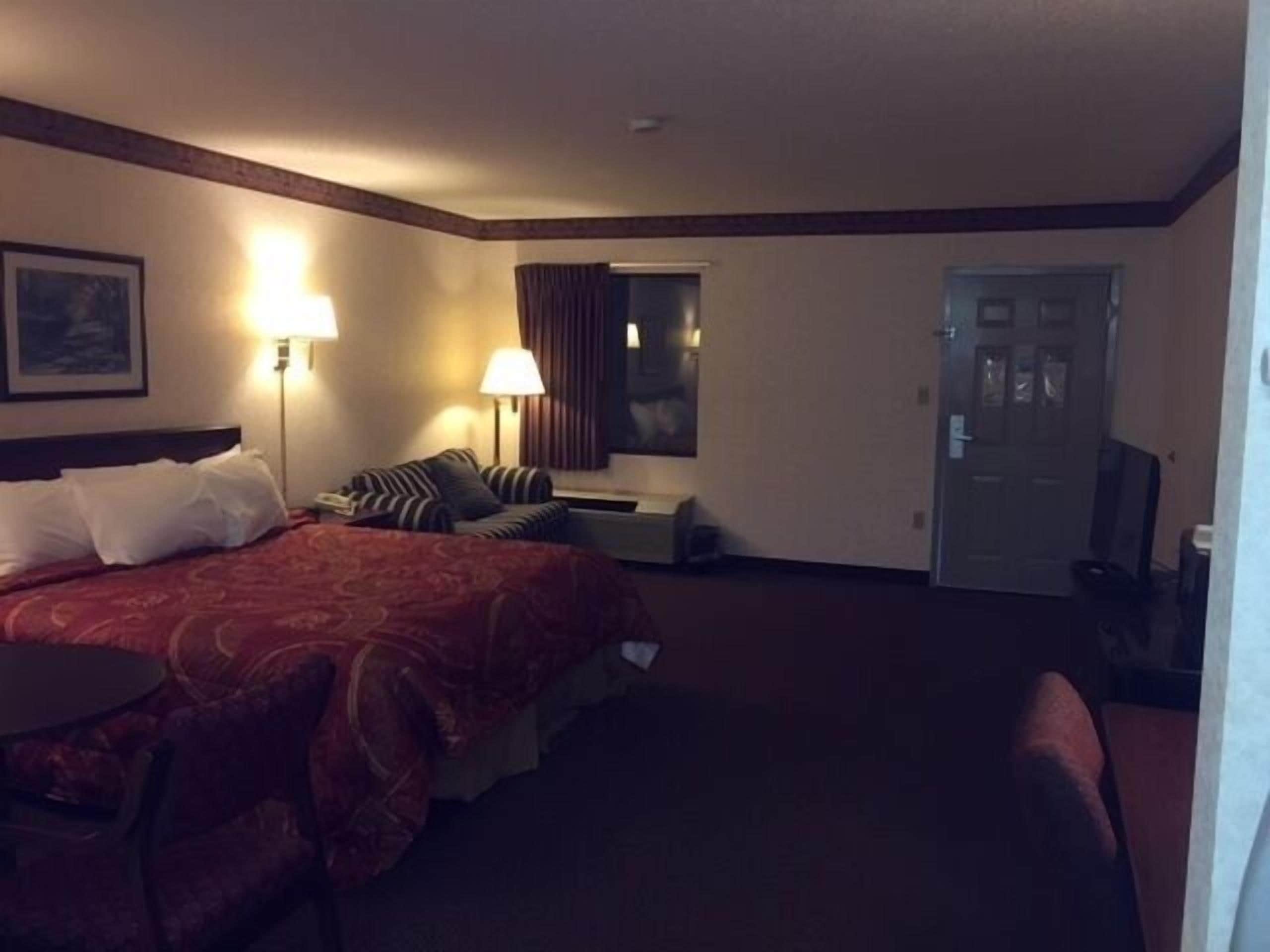 A hotel room with a large bed, two bedside lamps, a desk, a chair, and a door.