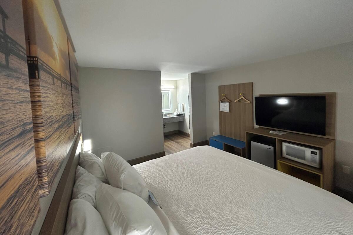 A hotel room with a bed, a television, a microwave, and a wooden wardrobe.