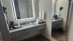 A bathroom with a large mirror, a sink, a hairdryer, and a coffee maker.
