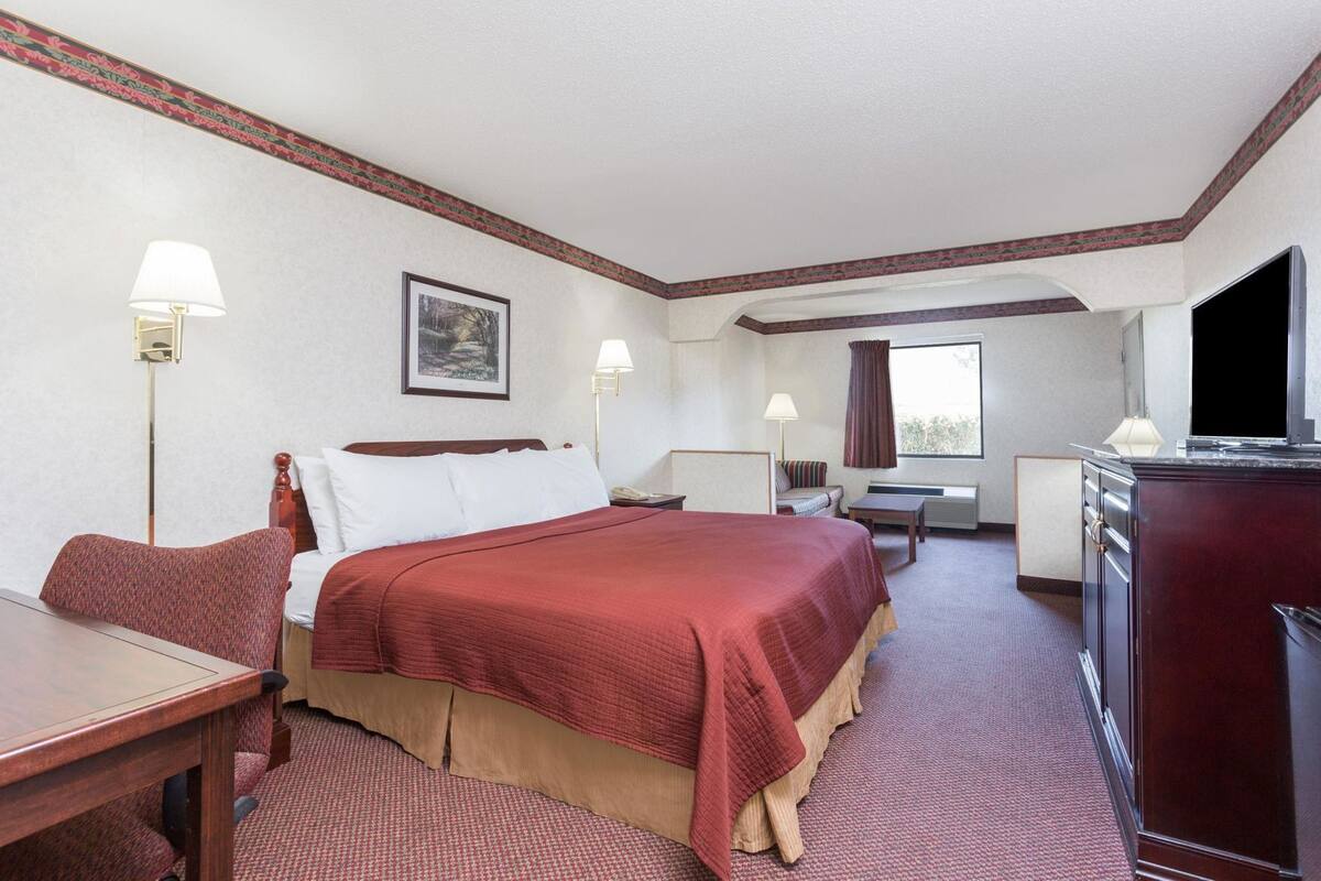 A hotel room with a bed, desk, chair, television, and a window.