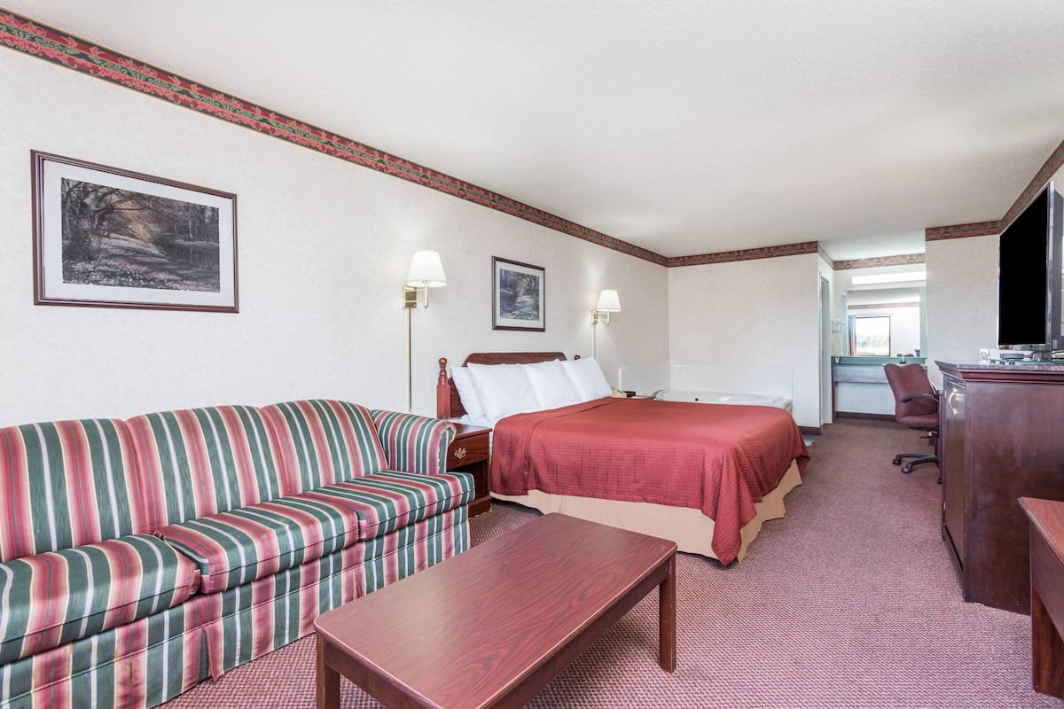 A hotel room with a striped sofa, a bed with a red bedspread, a wooden desk, two wall-mounted lamps, and framed pictures on the wall.