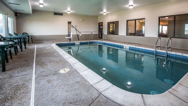 An indoor swimming pool with clear water, surrounded by a tiled deck and a few chairs.