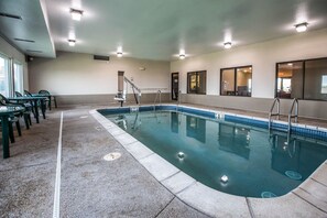 Una piscina interior amb aigua cristal·lina, envoltada per un solàrium emblumat i algunes cadires.