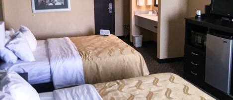 A hotel room with two beds, a desk, a television, and a bathroom.