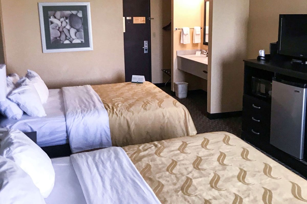 Ein Hotelzimmer mit zwei Betten, einem Schreibtisch, einem Fernseher und einem Badezimmer.