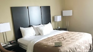 A hotel room with a large bed, two bedside tables with lamps, a nightstand with a phone, and a headboard with three panels.