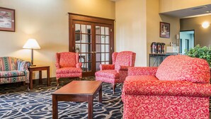 A hotel lobby with patterned carpet, red patterned sofas, a wooden coffee table, a striped sofa, and a lamp.