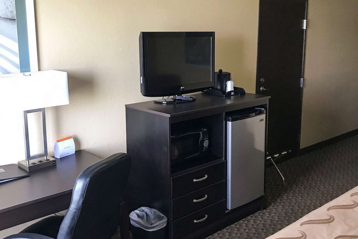 Ein Hotelzimmer mit Schreibtisch, Flachbildfernseher, Mikrowelle, Minikühlschrank, Stuhl und Mülleimer.