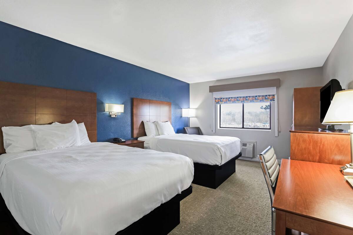 A hotel room with two beds, a desk, and a window with a view.