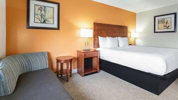 A hotel room with a bed, two bedside tables with lamps, a sofa, and two framed pictures on the walls.
