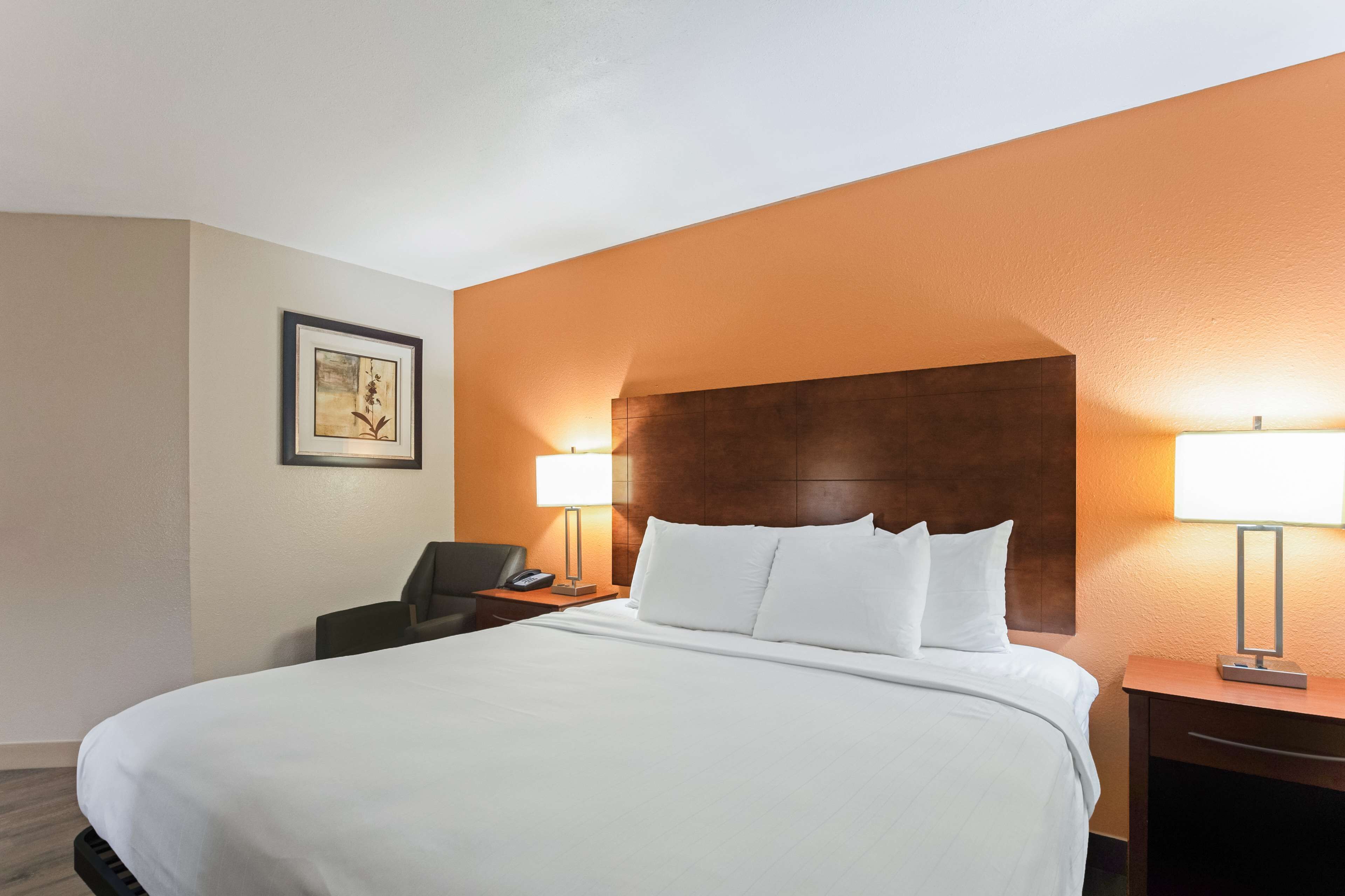 Habitación de hotel con una cama grande, dos lámparas de noche, un escritorio con una silla y un cuadro en la pared.