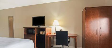 A hotel room with a bed, a desk with a computer, a lamp, a TV, and a wardrobe.