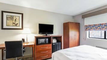 Ein Hotelzimmer mit Bett, Schreibtisch, Stuhl, Fernseher, Kleiderschrank und einem Fenster mit Jalousien.