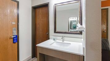 A hotel bathroom with a wooden door, a white sink, and a mirror.