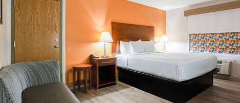 A hotel room with a bed, bedside tables, a desk, a chair, and a wardrobe.