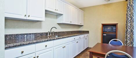 A compact kitchen with white cabinets, a granite countertop, and a built-in microwave.