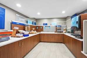 A modern kitchen with wooden cabinets, a fruit station, a coffee machine, and a 'Good Morning' sign. - Holiday Inn Express Hotel & Suites Wabash by IHG (Wabash)