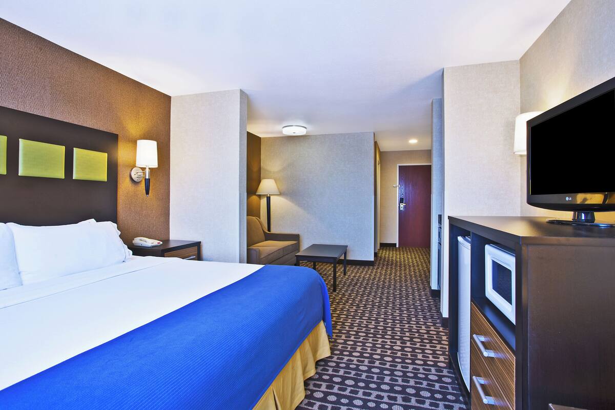 A hotel room with a bed, bedside table, lamp, TV, and a patterned carpet.