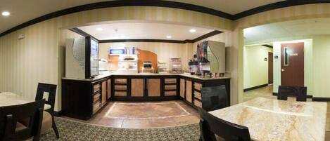 A hotel room with a curved layout, a kitchen area with a central island, and a dining area with a marble table.