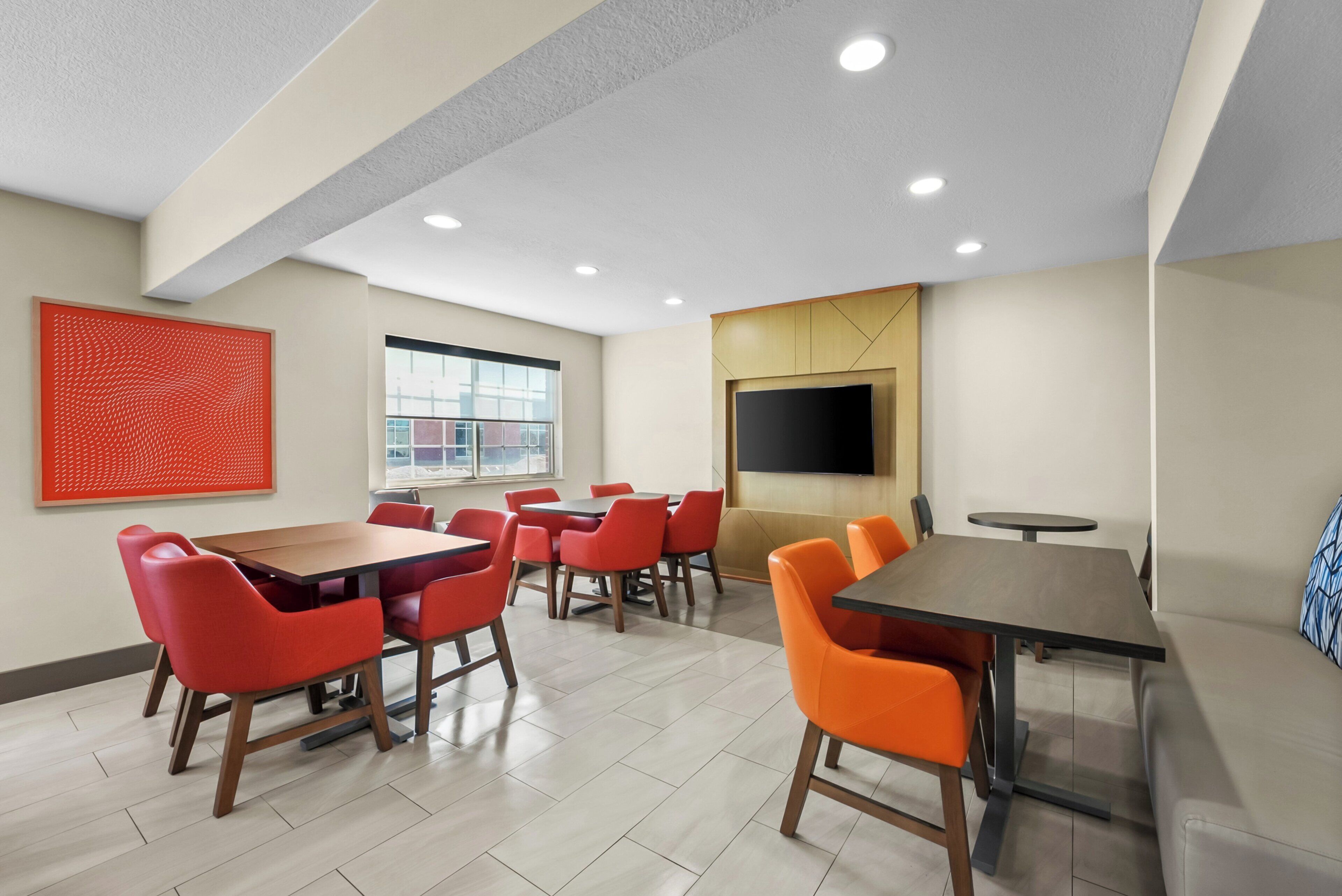 A modern conference room with a large table, red and orange chairs, a flat-screen TV, and a window with a view.
