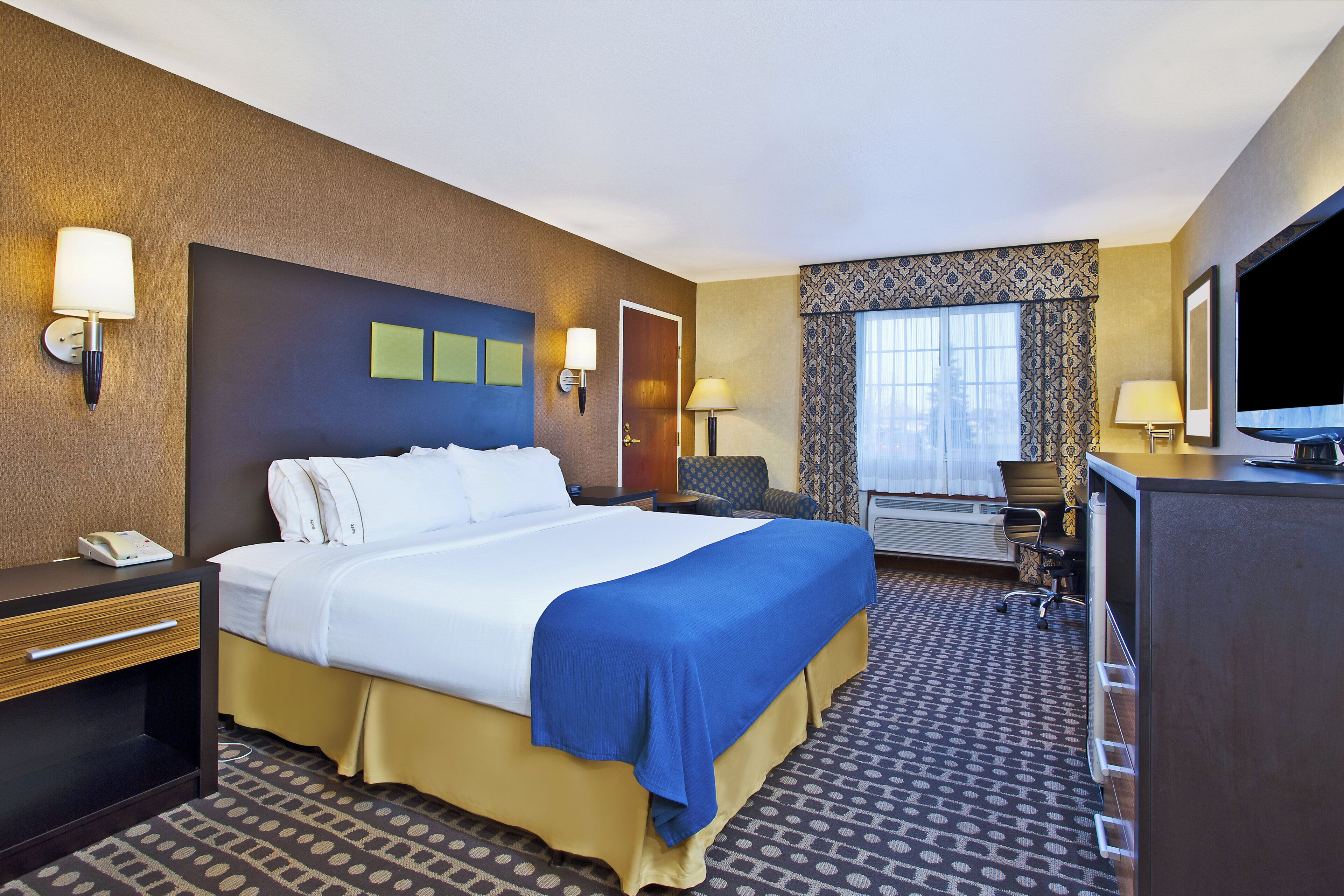 Een hotelkamer met een bed, nachtkastjes, een bureau, een stoel, een televisie en een raam met gordijnen.