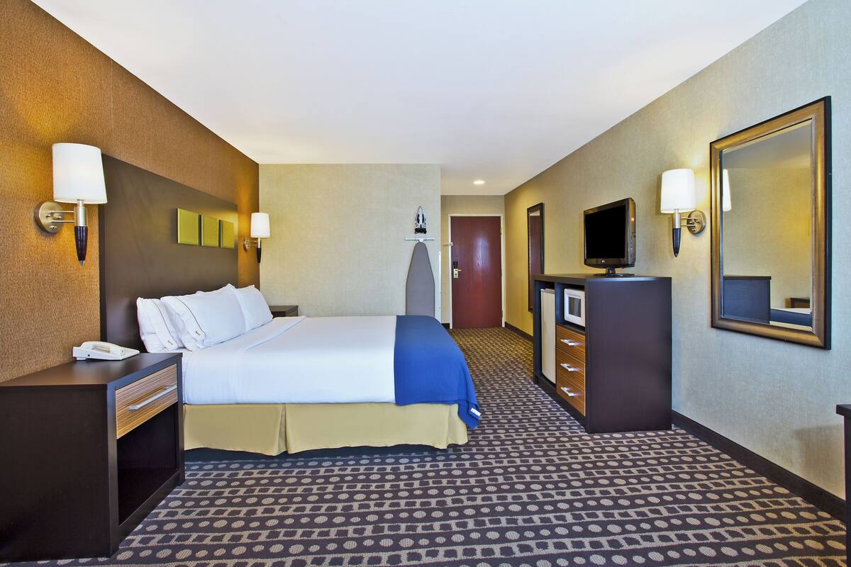A hotel room with a bed, a desk, a dresser, a television, and a mirror.