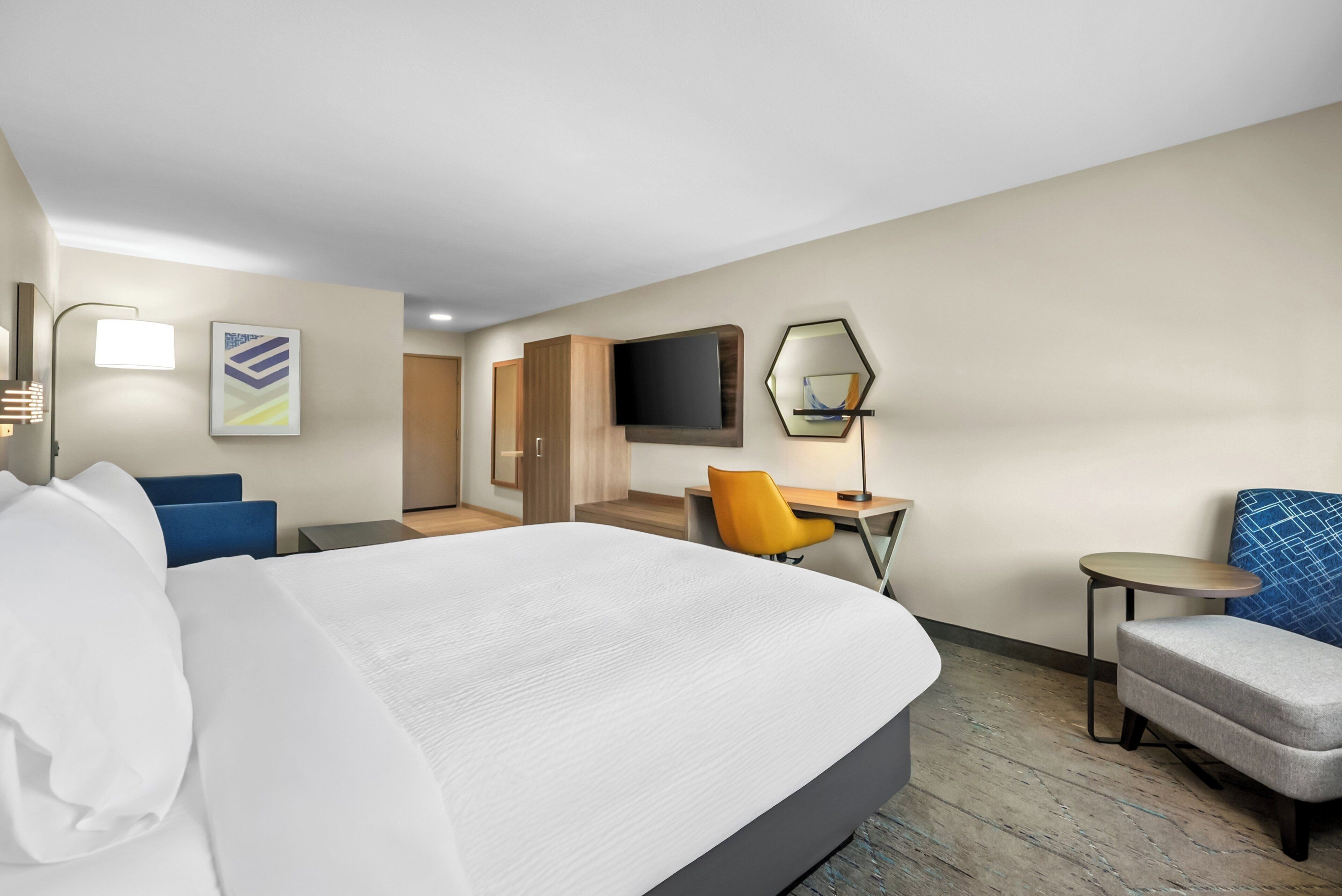 Una habitación de hotel con cama, escritorio, silla, televisión y obras de arte en las paredes.