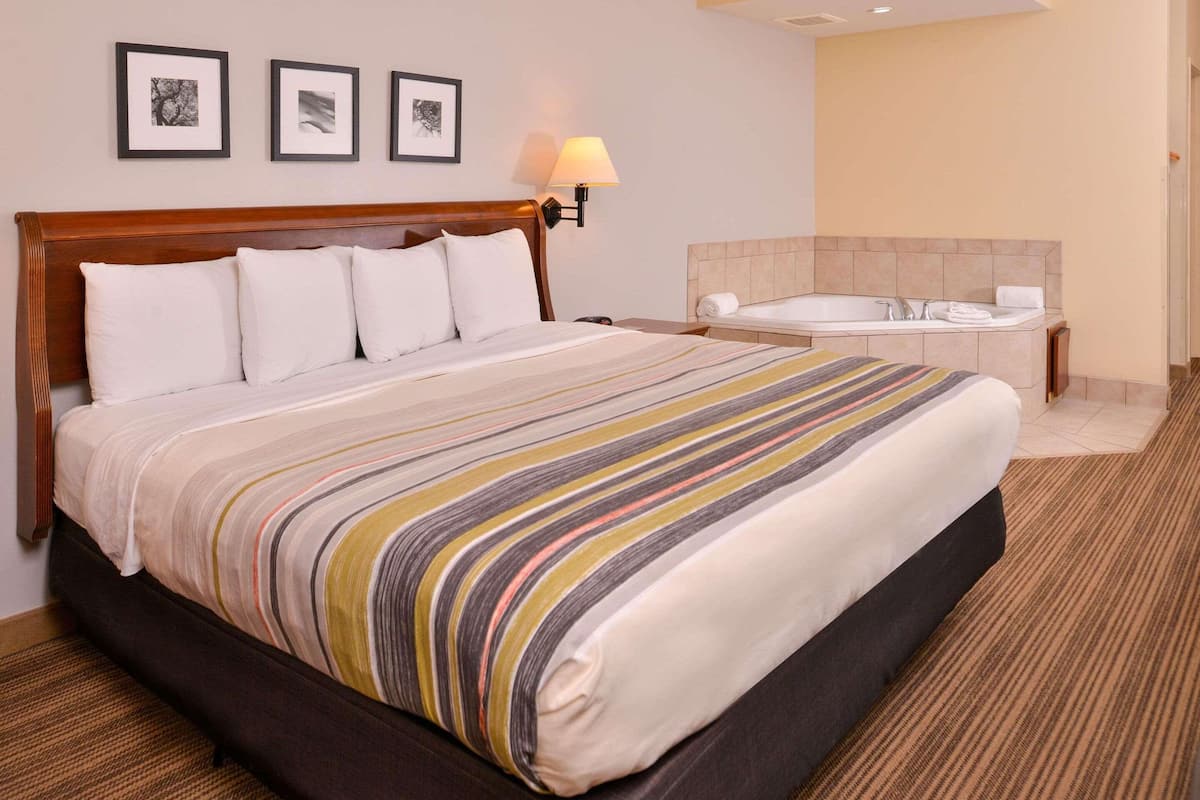 Ein Hotelzimmer mit einem großen Bett, einem separaten Badezimmer mit Badewanne und gerahmten Bildern an der Wand.