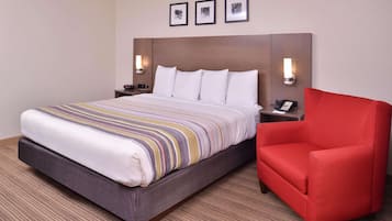 Quarto de hotel com uma cama grande, uma poltrona vermelha e cabeceira com luzes fixadas na parede.