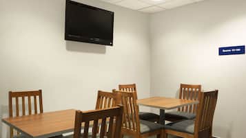 Un salón de conferencias con televisor de pantalla plana montado en la pared, mesas y sillas de madera, y un letrero que indica el número de la sala.