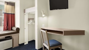 Ein Hotelzimmer mit Schreibtisch, Stuhl, Fernseher und einem Fenster mit Vorhängen.