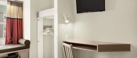 Habitación de hotel con escritorio, silla, televisión y ventana con cortinas.