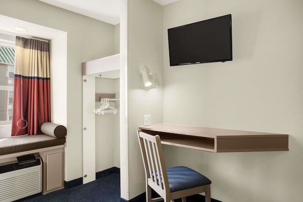 Une chambre d’hôtel équipée d’un bureau, d’une chaise, d’une télévision et d’une fenêtre avec des rideaux.