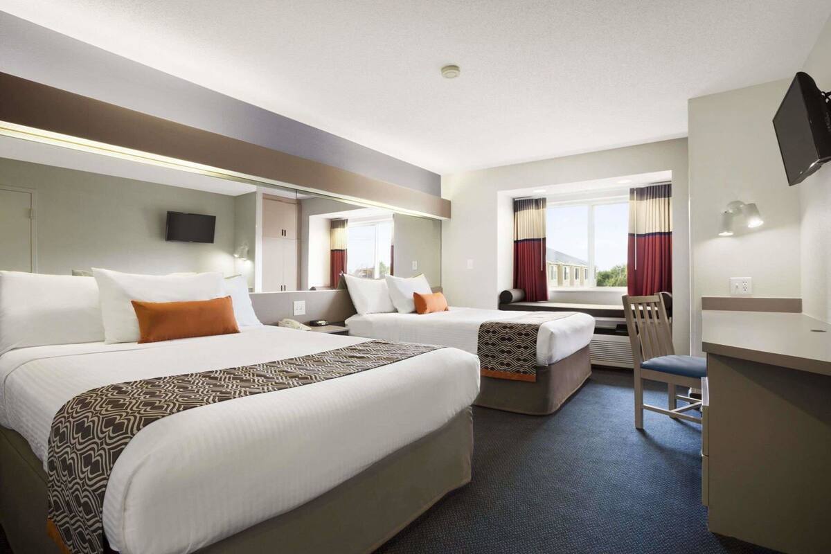 Une chambre d’hôtel avec deux lits, un bureau, une chaise, une télévision et une fenêtre avec des rideaux.