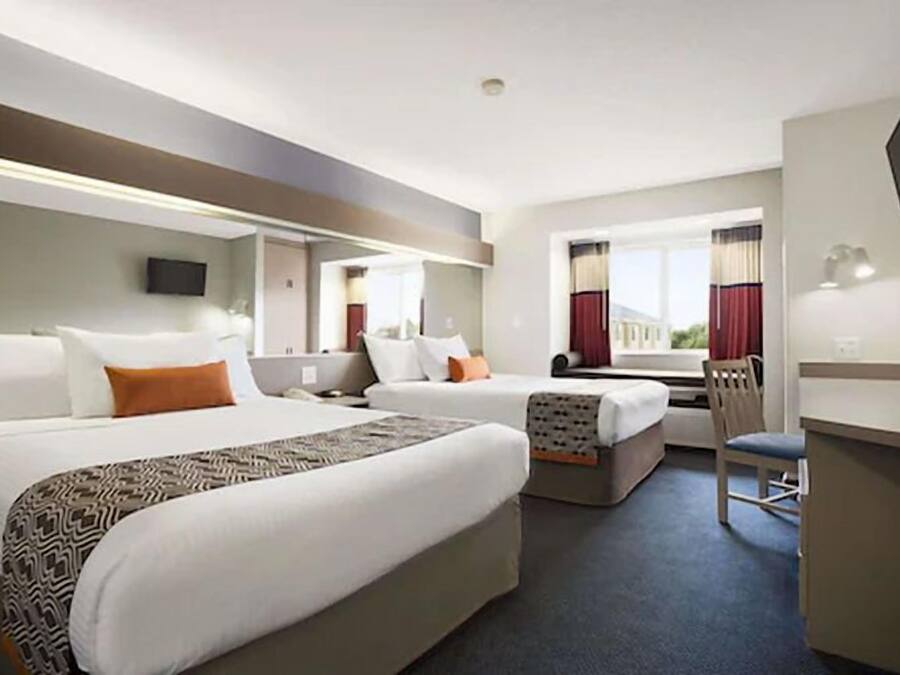 A hotel room with two beds, a desk, a chair, and a TV.